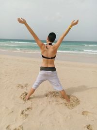 Rear view of woman with arms raised standing at beach