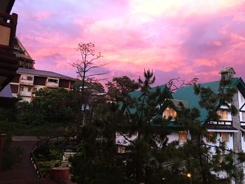 Houses and trees by lake against sky at sunset