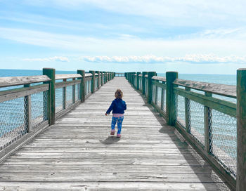 Rear view of woman on pier over sea against sky