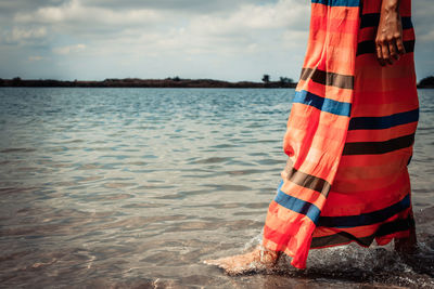 Unrecognizable woman in a dress walking through the sea in summer day,