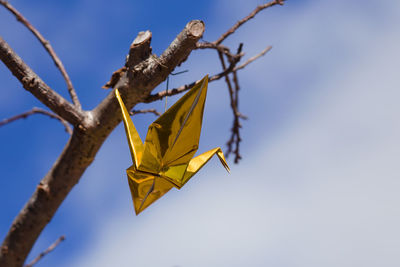 Low angle view of golden foil crane hanging on branch against sky