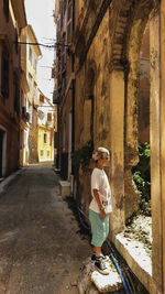 Side view of boy looking at abandoned building while standing in alley 