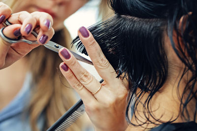 Cropped hands of hairdresser cutting hair in salon
