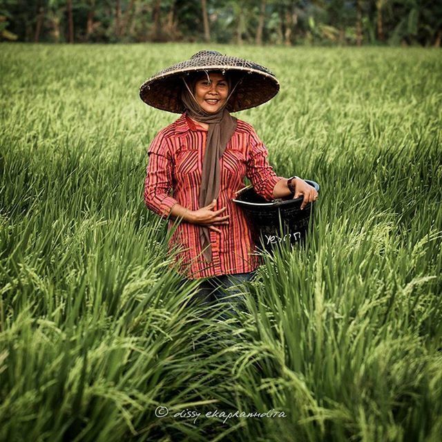 grass, field, grassy, person, looking at camera, growth, front view, portrait, smiling, green color, focus on foreground, plant, red, lifestyles, sitting, leisure activity, nature, young adult