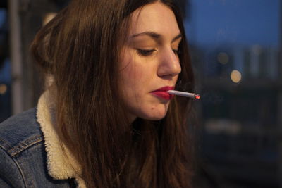 Close-up of young woman smoking cigarette in city at night