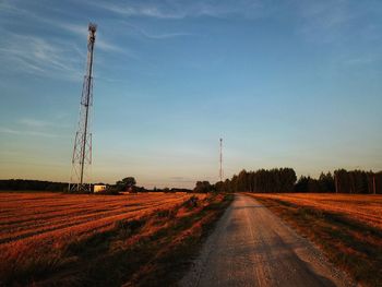 Dirt road amidst field against sky