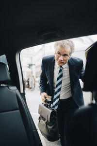 Mature male entrepreneur getting in taxi during business trip