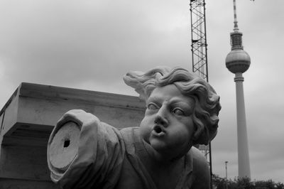 Low angle view of communications tower and sculpture against buildings