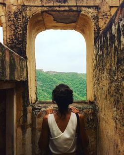 Rear view of woman looking through window of old ruins