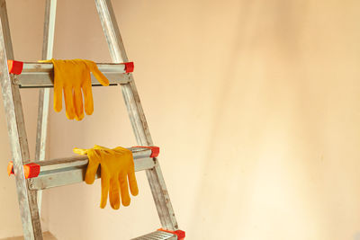 Yellow work gloves on a stepladder against the background of an empty wall. 