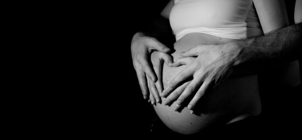 Midsection of man touching pregnant woman belly against black background