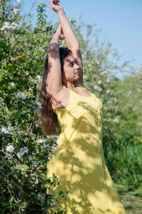 Side view of young woman standing against trees