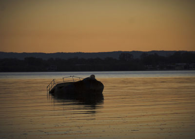 Silhouette boat moored in lake against sky during sunset