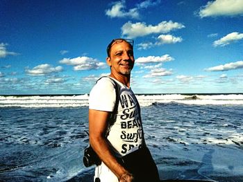 Portrait of smiling man standing at beach against sky