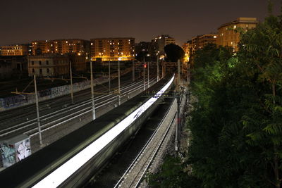 High angle view of train moving on railroad tracks in illuminated city at night