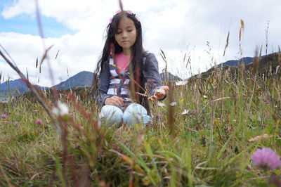 Low angle view of girl touching flower sitting on land against sky