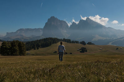 Rear view of woman walking on field towards mountains