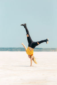 Woman with arms raised on beach against sky