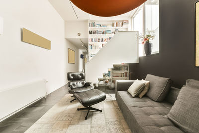 Interior design of lounge area with comfortable sofa and leather armchair in modern apartment with white walls and tiled floor