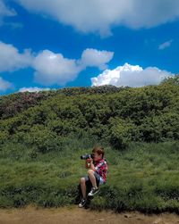 Friends photographing while standing on grass in forest against sky