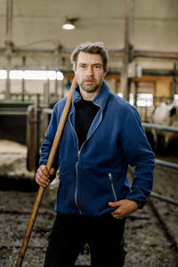 Farmer standing with wooden stick at cattle farm