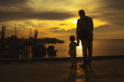 Silhouette friends standing on beach against sky during sunset