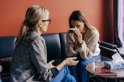 Female patient sitting on sofa and crying while psychotherapist consoling and advising 