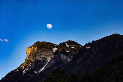 Low angle view of moon over mountain against blue sky