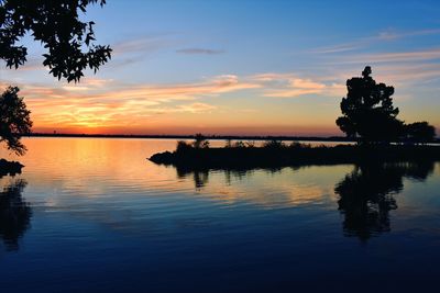 Silhouette trees by sea against sky during sunset