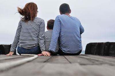 Rear view a family of three, dressed in blue striped longsleeve, holding hands, a child in between