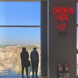 Rear view of people standing by window with text against cityscape