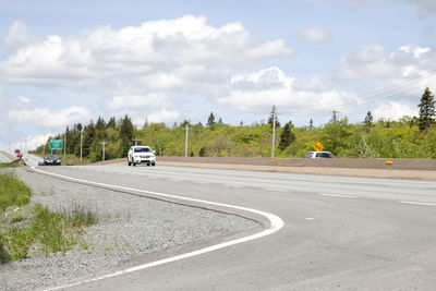 Vehicles on road against cloudy sky