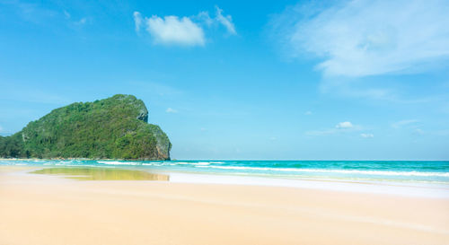 Scenic view of brown sand beach  on blue sea against sky