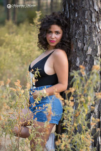 Portrait of smiling young woman standing on tree trunk