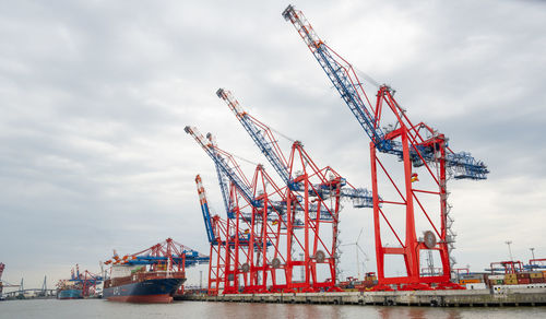 Cranes at commercial dock against sky