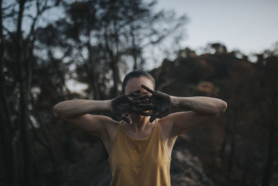 Woman hiding face behind hands black with ash in burnt forest