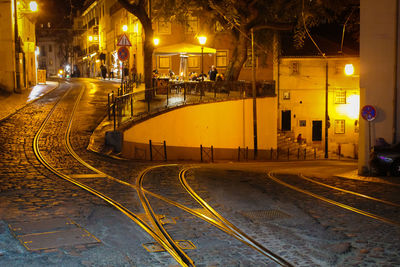 Illuminated railroad tracks by buildings in city at night