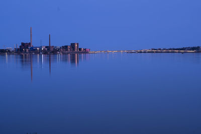 Reflection of buildings in sea against clear blue sky