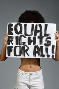 Midsection of woman holding banner while standing against gray background