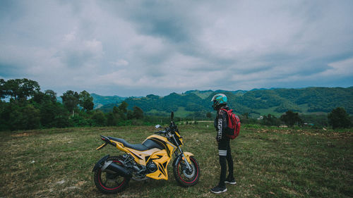 Man standing by bicycle on field against sky