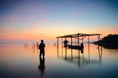 Silhouette man standing in lake against sky during sunset