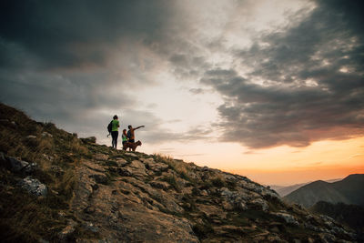 People on rock against sky during sunset