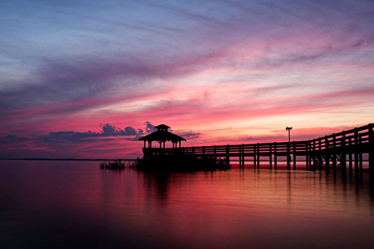 SILHOUETTE BUILT STRUCTURE BY SEA AGAINST SKY DURING SUNSET