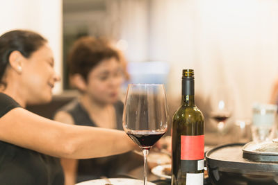 Wine bottle and glasses on dinner table with woman in background.