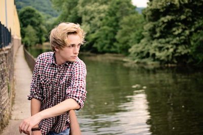 Handsome young man leaning on railing at footbridge over river