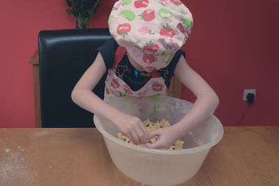 Girl wearing apron mixing batter in container on table at home