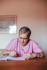 Front view of a senior woman with alzheimer's mental health issues painting on a notebook inside her home