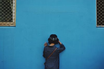 Rear view of young woman wearing hat while standing by blue wall