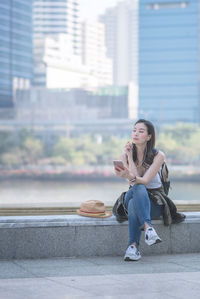 Young woman sitting on camera in city