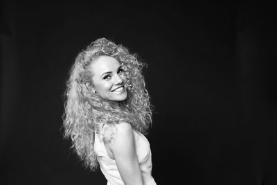 Portrait of smiling woman with curly hair standing against black background